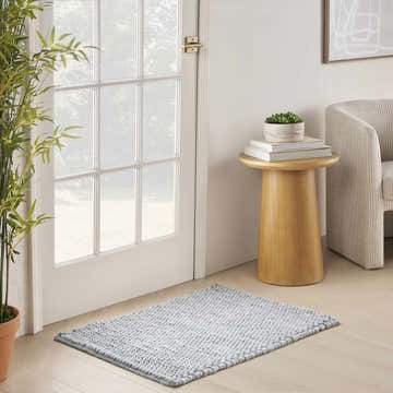 Entryway scene with a denim DKNY Pure Knots rug, light wood floors, white door, and mid-century modern decor.