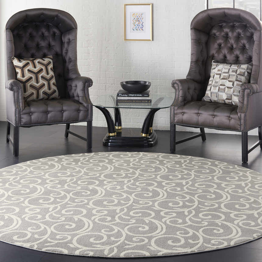Living room scene with a round Nourison Grafix Grey rug, two dark wingback chairs, and a glass coffee table.