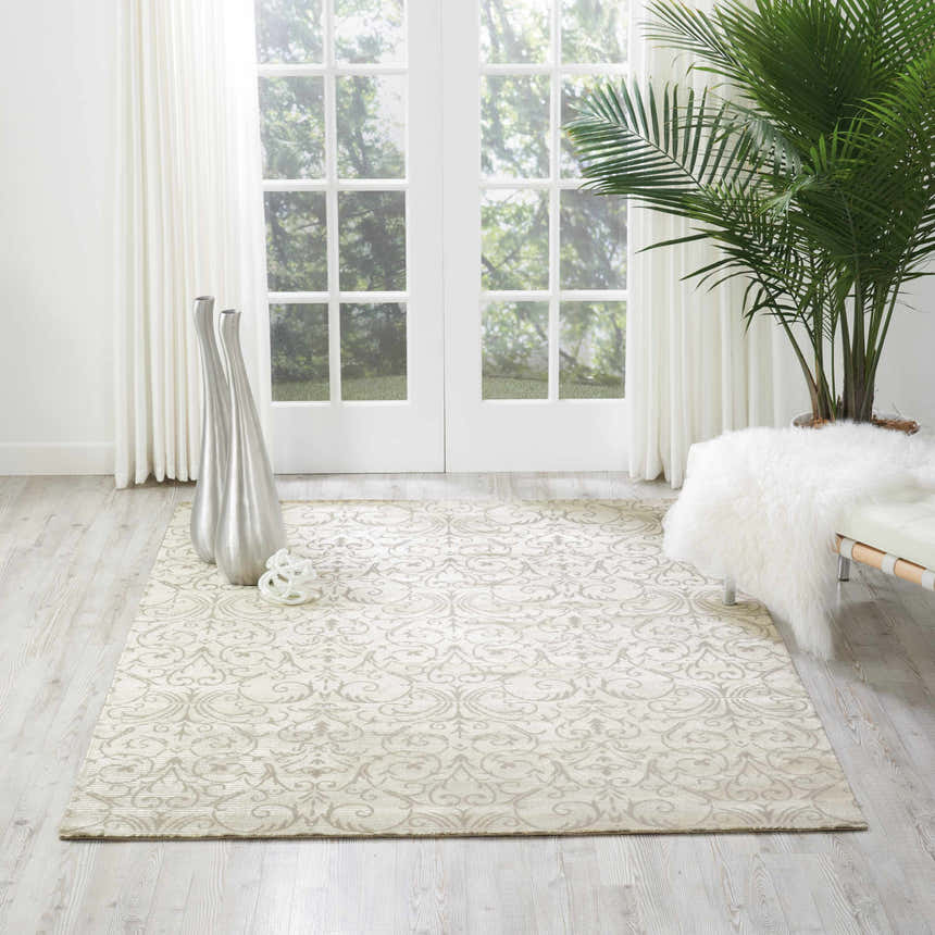 Sunlit room with Nourison Luminance Opal Vintage rug, silver vases, palm tree, and white bench. Serene, light-filled space.