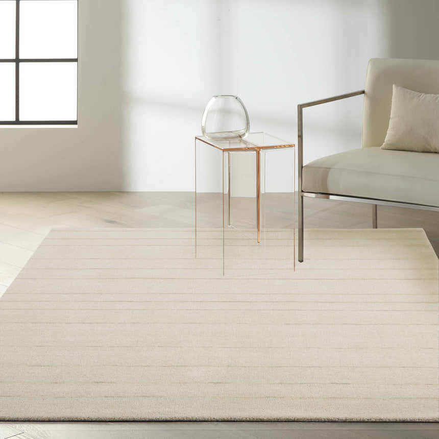Minimalist living room scene with Calvin Klein Halo Ivory rug, clear side table, and modern chair.