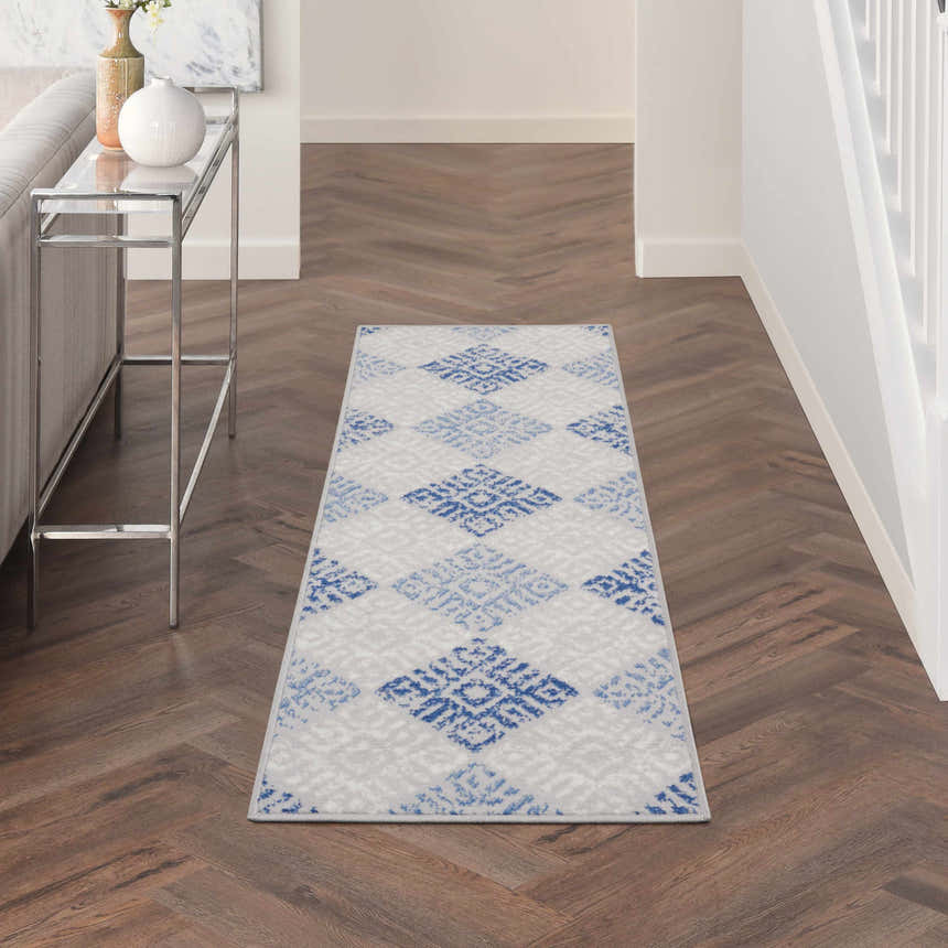 Hallway scene with Nourison Whimsicle Grey Blue rug, herringbone wood floors, console table, and white walls.