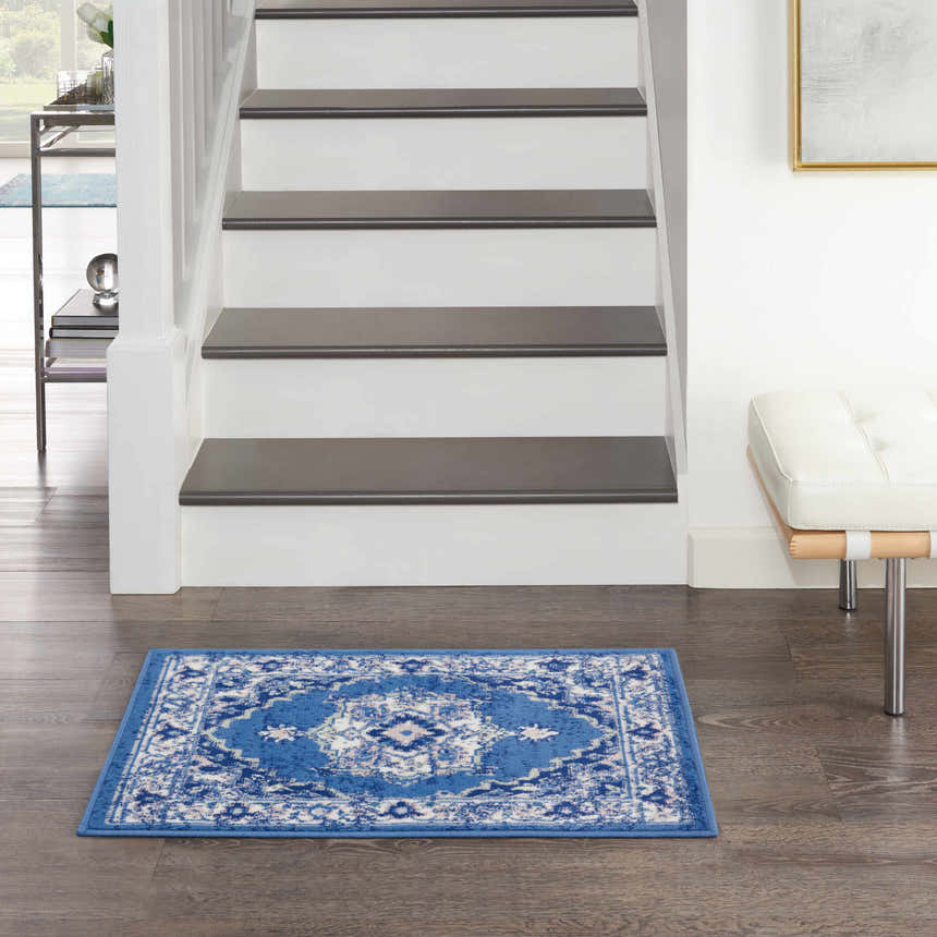 Entryway scene with a Nourison Whimsicle Navy Farmhouse Indoor Area Rug on dark wood floors by stairs and a white bench.