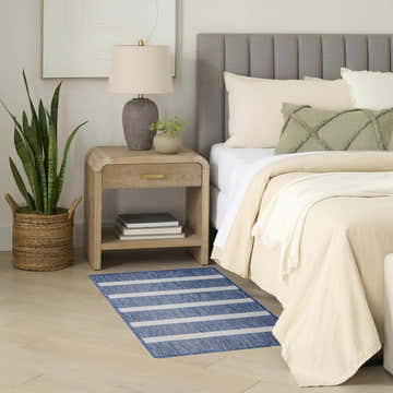 Bedroom scene with a Nourison Positano Navy Ivory rug, wood nightstand, and neutral bedding.