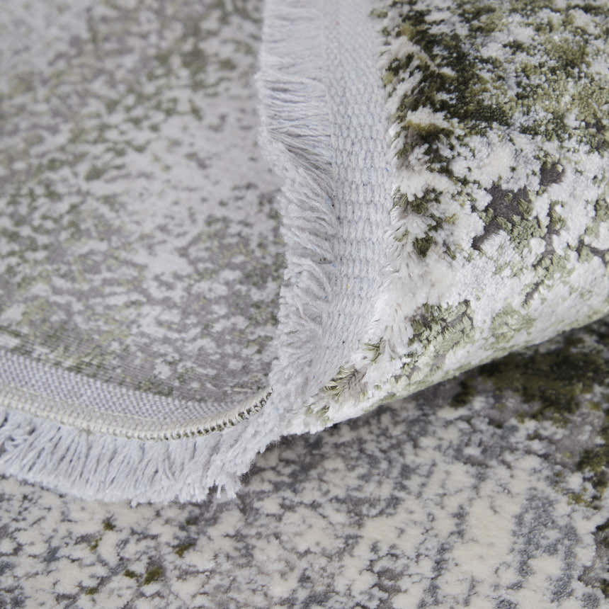 Close-up of Feizy Cadiz Modern Ikat rug showing gray, green, and silver abstract pattern and fringe detail. Fold