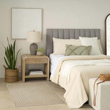 Bedroom scene with a Nourison Charm Beige Ivory rug, wood nightstand, gray headboard, and neutral decor.