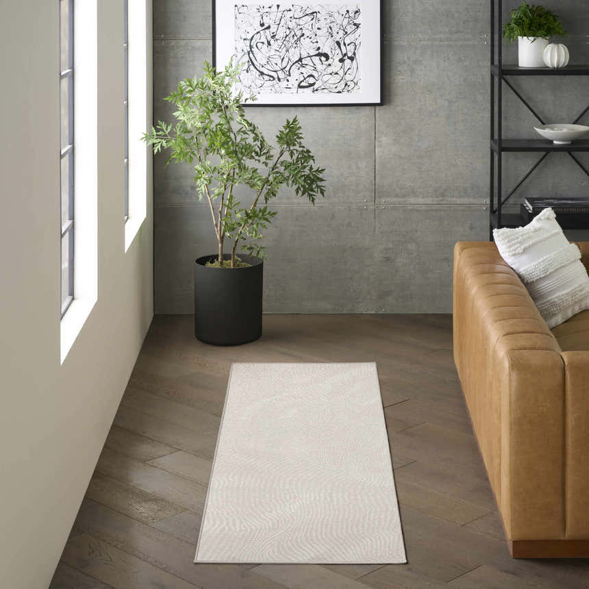 Modern living room with a DKNY Central Park West Ivory rug, tan leather sofa, and dark wood floors.