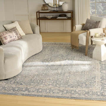 Living room scene with a light blue vintage Nourison Retreat area rug, curved sofa, and accent chair.