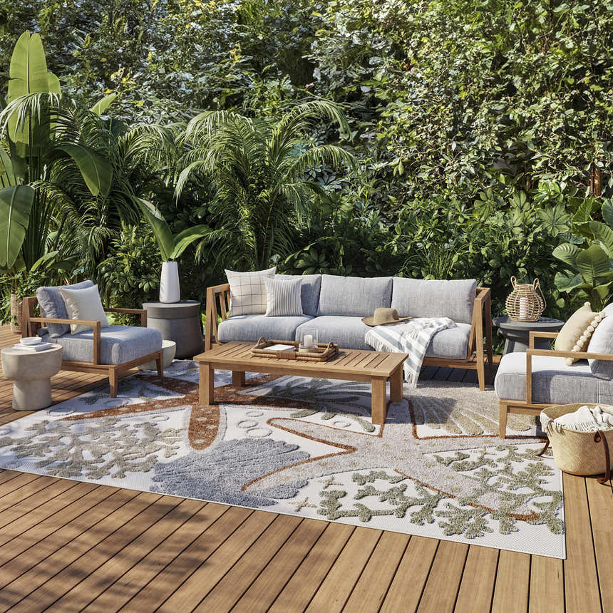 Outdoor patio scene with gray furniture on a Nourison Aloha Ivory Multicolor Area Rug. Lush green plants surround the space.