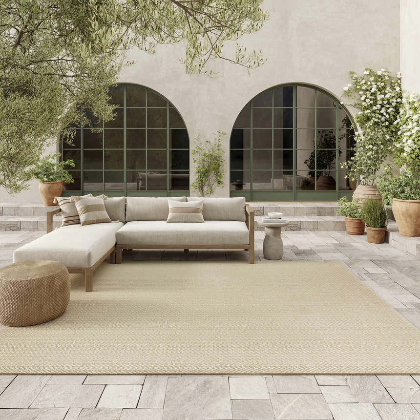 Cream Nourison Tulum outdoor rug on a patio with a sectional sofa and potted plants.