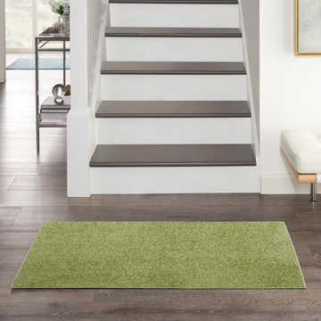 Entryway scene with a Nourison Essentials Green Outdoor Area Rug on dark wood floors, stairs in the background.
