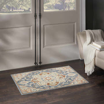 Entryway scene with Nourison Maison Blue Ivory Vintage rug, dark wood floors, and a cream-colored chair with a throw.