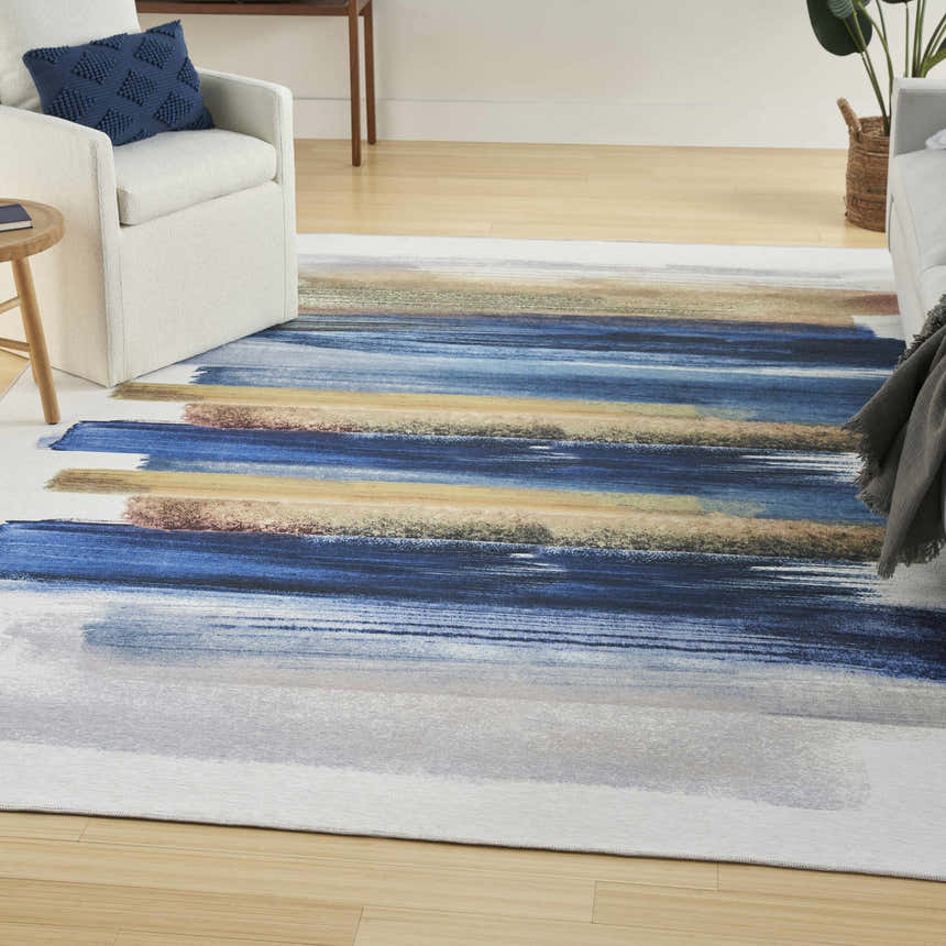 Living room scene with a Nourison Blue Multicolor Modern Indoor Washable Area Rug, white chairs, and light wood floors.