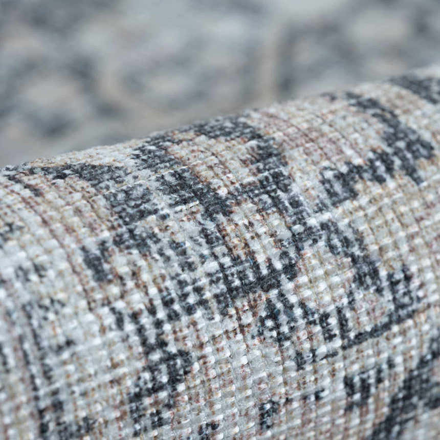 Close-up of the textured weave of a rolled Hedda Boutique Washable Rug in dark gray, gray, and nutmeg. Fold
