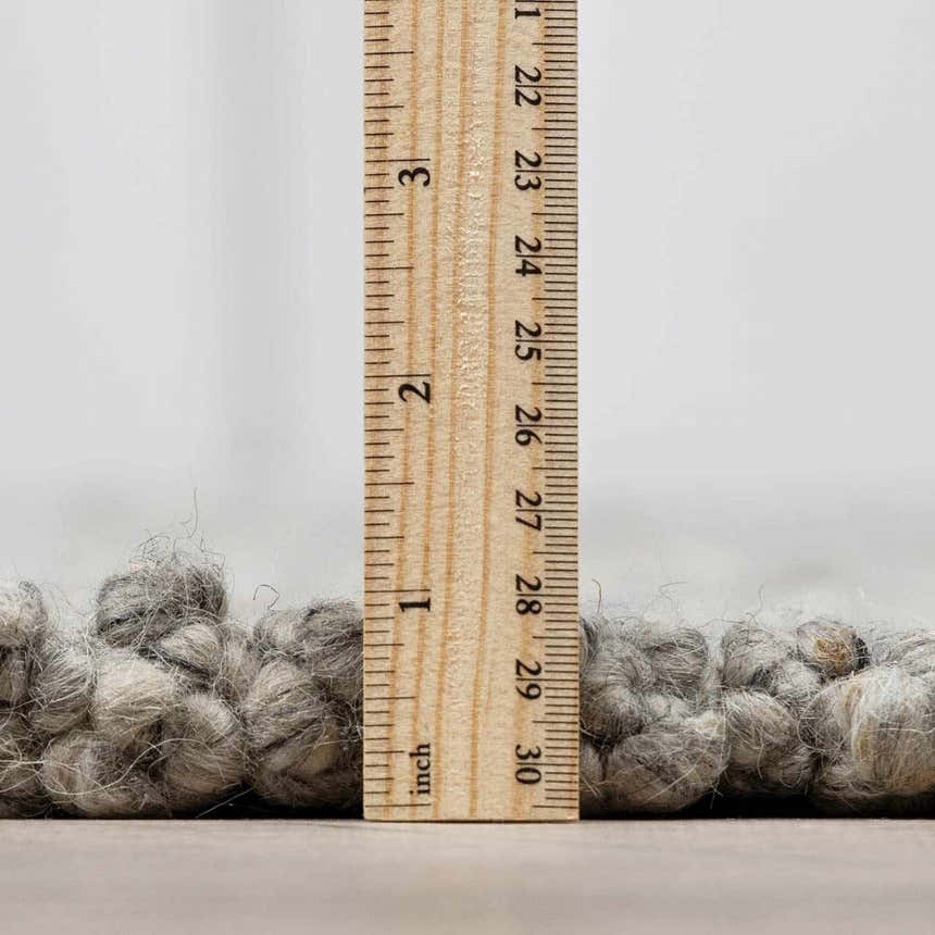 Close-up of the Basiao Area Rug showing the charcoal and cream wool texture and pile height with a ruler. Pile