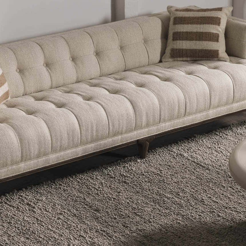 Living room scene with a neutral tufted sofa and the charcoal Basiao Area Rug, creating a cozy, textured look. Styleshot
