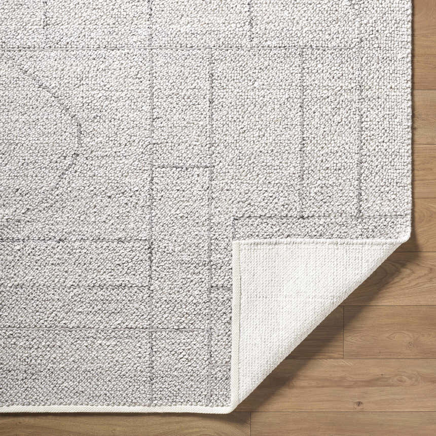 Close-up of the hand woven Brenta Area Rug. Gray, light silver, and sage hues with a geometric pattern. Fold