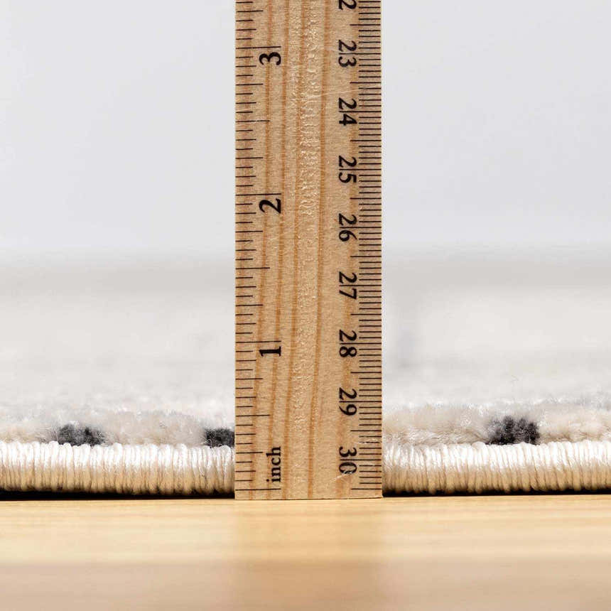 Close-up of the New Burdette Area Rug pile height, showing charcoal geometric pattern on off-white. Pile