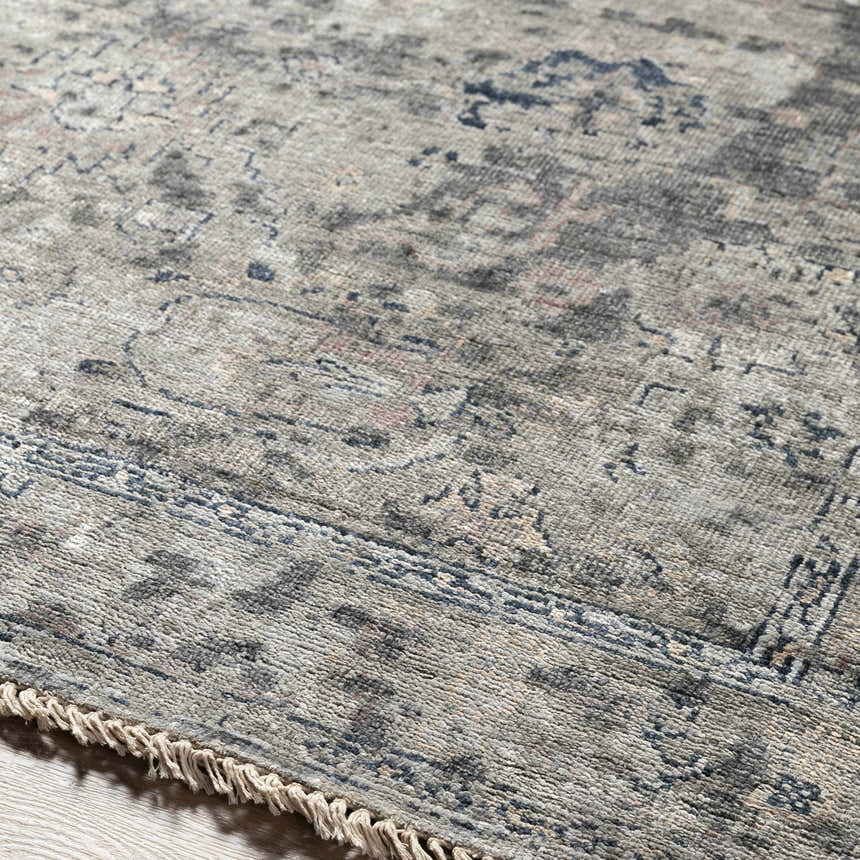 Close-up of the hand-knotted Ballantrae Premium Rug. Beige, charcoal, and blue tones with a traditional oriental pattern and fringe. Texture