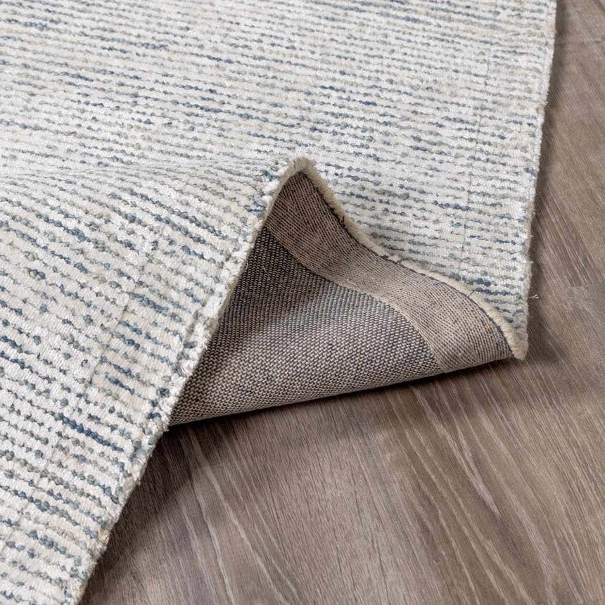 Close-up of the Orcas Hand Tufted Wool-Blend Rug - Slate, showing the blue and cream striped design and backing texture. Fold