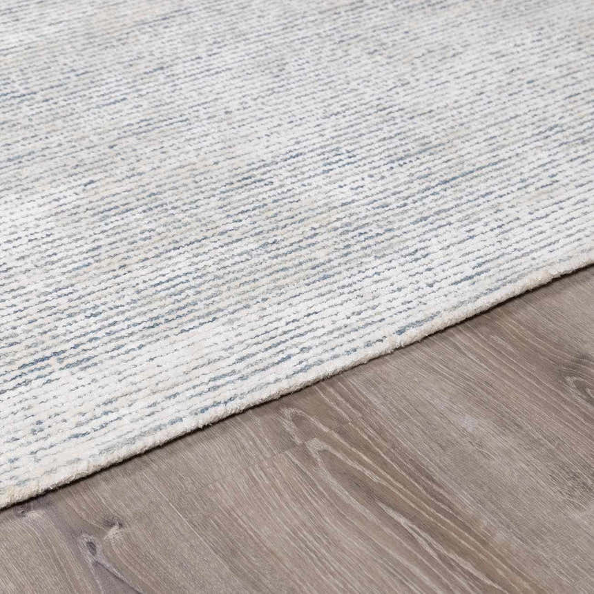 Close-up of Orcas Hand Tufted Wool-Blend Rug - Slate. Cream rug with subtle blue stripes on wood floor. Pile