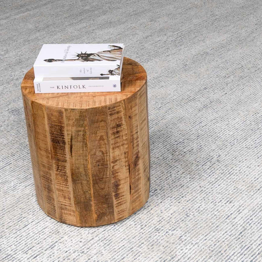 Close-up of the slate Orcas Hand Tufted Wool-Blend Rug with a subtle striped pattern and a wood stump side table. Styleshot