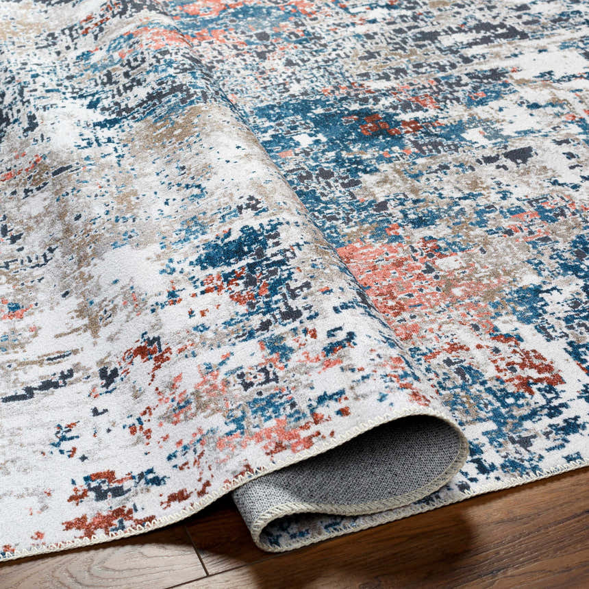 Close-up of Ballyshannon Washable Area Rug showing abstract design in dark gray, denim, nutmeg, and silver on wood floor. Fold