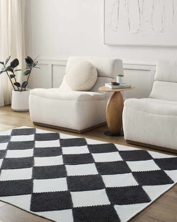 Living room scene with Bosley Black Washable Area Rug, two cream chairs, wood side table, and modern art. Black and white checkered rug. Roomscene-Rectangle