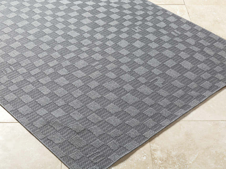 Close-up of the gray Arifah Area Rug featuring a woven checkerboard pattern on a beige tile floor. Corner