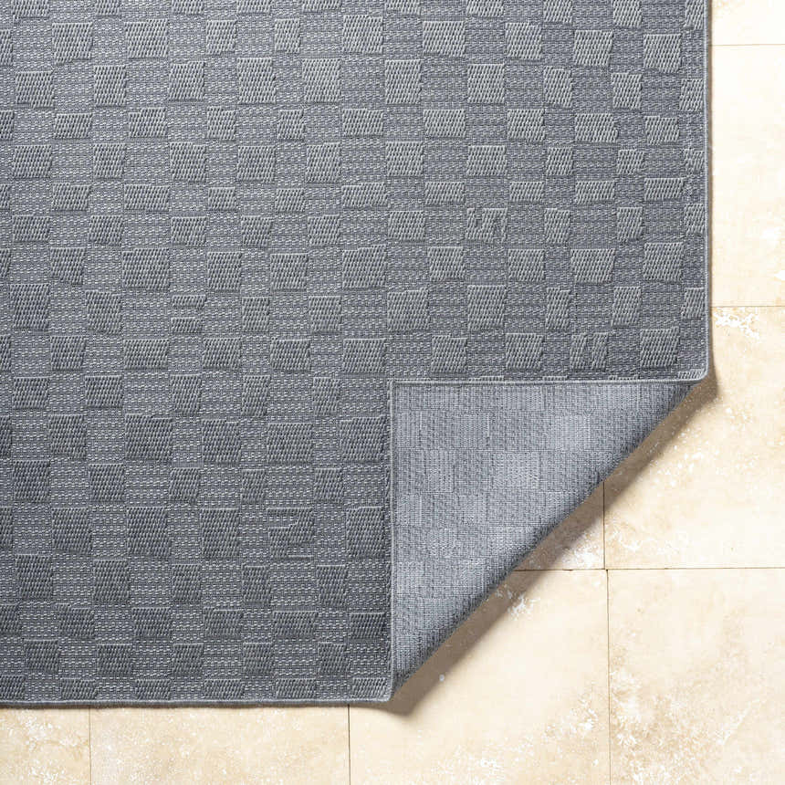 Close-up of the gray Arifah Area Rug showing its woven checkerboard pattern and texture on a light tile floor. Fold