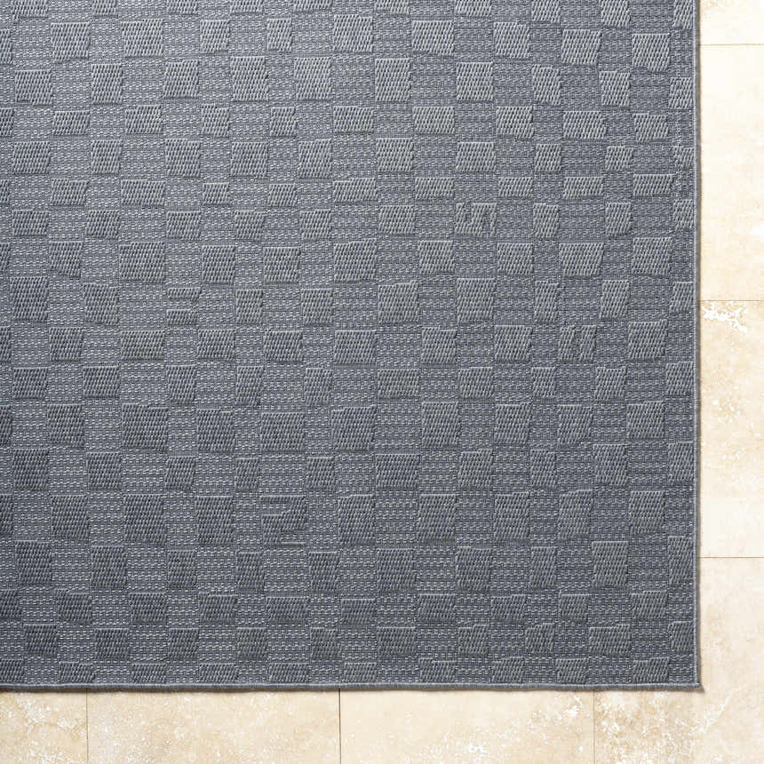 Close-up of the gray Arifah Area Rug showing a woven checkerboard pattern and texture on a light stone tile floor. Corner