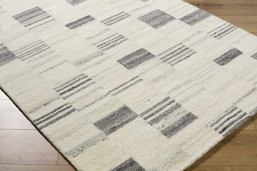 Close-up of the Max Handmade Becki Owens x LIVABLISS BOMX-2305 Area Rug. Cream wool rug with ash, blue, and charcoal geometric pattern. Corner
