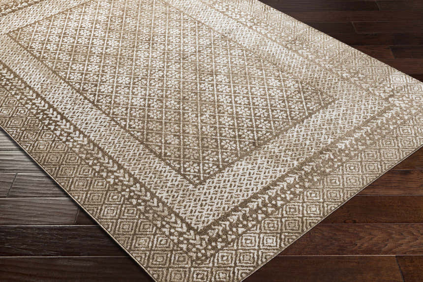 Close-up of the Caditaan Washable Area Rug. Brown and cream rug with a traditional geometric pattern on dark wood floors. Corner