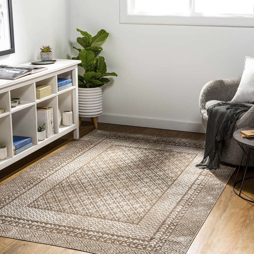 Living room scene with a brown and cream Caditaan Washable Area Rug, white shelving unit, gray chair, and wood floors. Roomscene-Rectangle