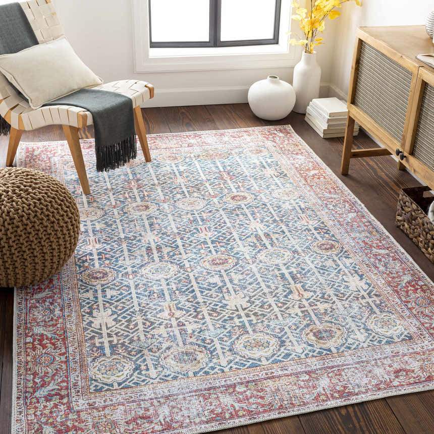 Sunlit living room with a Rust Catadupa Distressed Washable Area Rug, chair, and wooden cabinet. The rug features blue, gray, and red tones. Roomscene-Rectangle