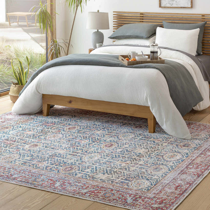Bedroom scene with a Rust Catadupa Distressed Washable Area Rug. The rug has a blue, gray, and red vintage Persian-style design. Roomscene-Rectangle
