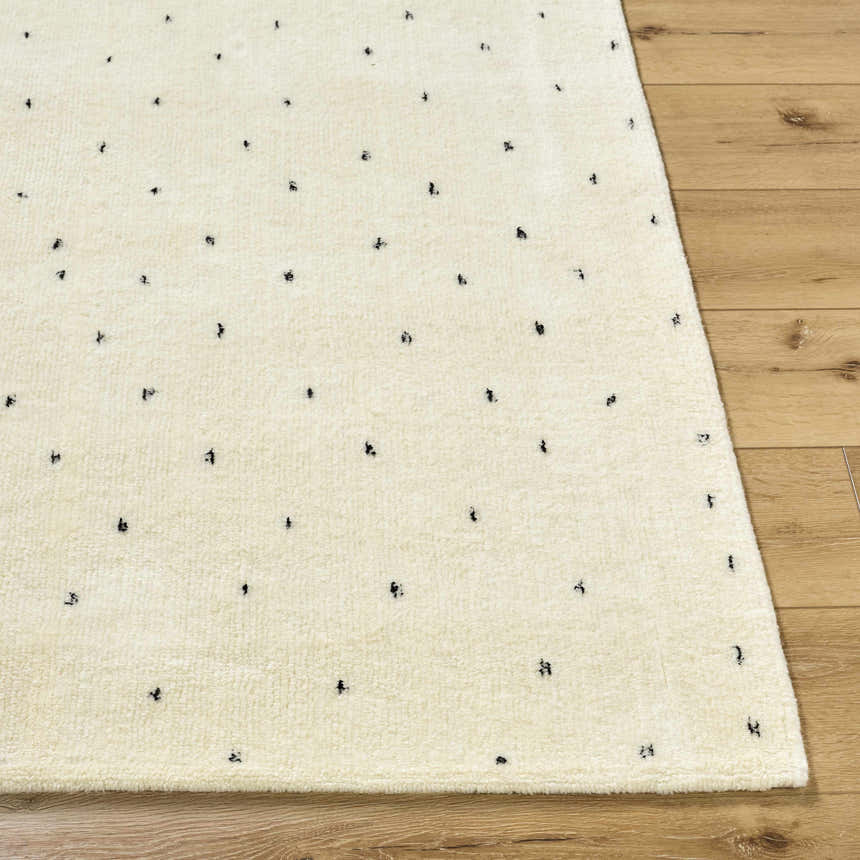 Close up of the ivory Cirila Dotted Wool Rug showing wool texture and charcoal dots on a wood floor. Front