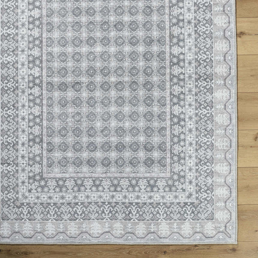 Close-up of the Rainier Machine Woven Washable Area Rug showing its farmhouse-style geometric pattern and off-white, pale blue, sage, and tan colors. Corner
