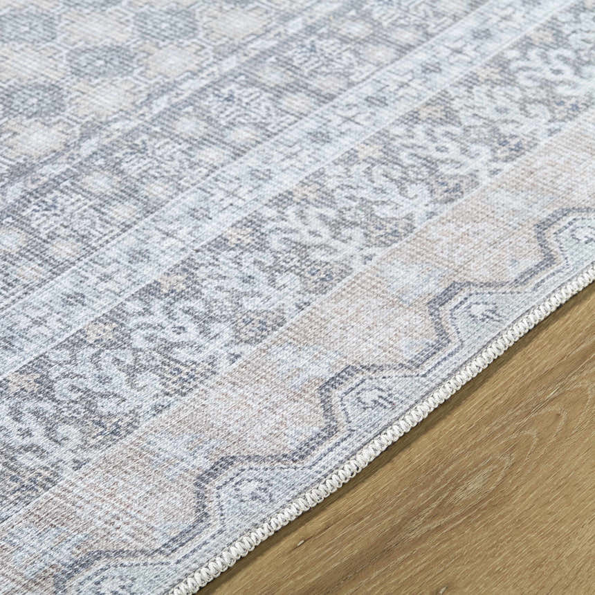 Close-up of Rainier rug showing traditional pattern in green, olive, pale blue, and white on wood floor. Texture