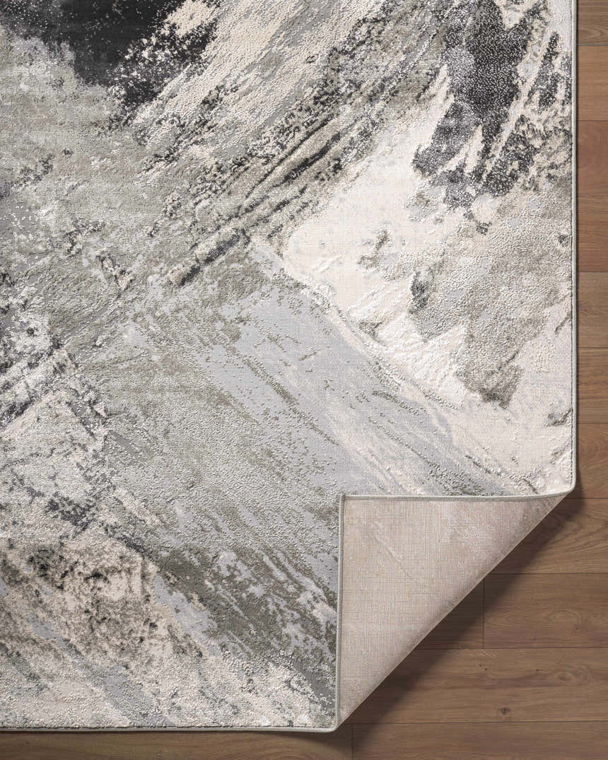 Close-up of the Chaeli Area Rug. Abstract design in beige, black, charcoal, ivory, and light slate. Machine woven texture. Fold