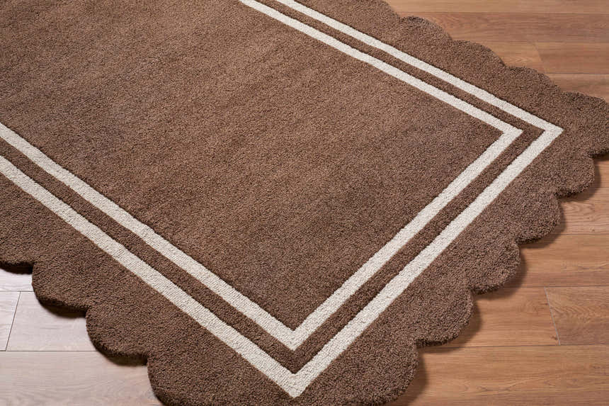 Close-up of a hand-tufted Chogan Chocolate Brown Area Rug. The wool rug has a scalloped edge and a double stripe border. Corner