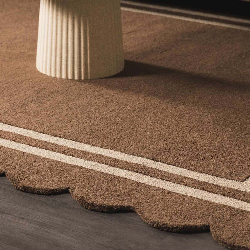 Close-up of the hand-tufted Chogan Chocolate Brown Area Rug, featuring a scalloped edge and cream-colored stripes. Roomscene-Rectangle