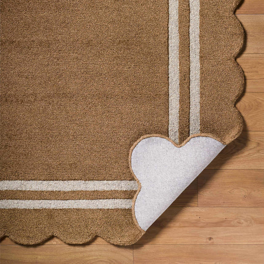 Close-up of the hand-tufted Chogan Umber Area Rug. Features a scalloped edge, umber color, and off-white stripes on 100% wool. Fold