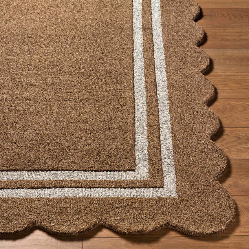 Close-up of the Chogan Umber Area Rug. Hand-tufted wool rug with umber color, white border, and scalloped edge. Contemporary style. Front
