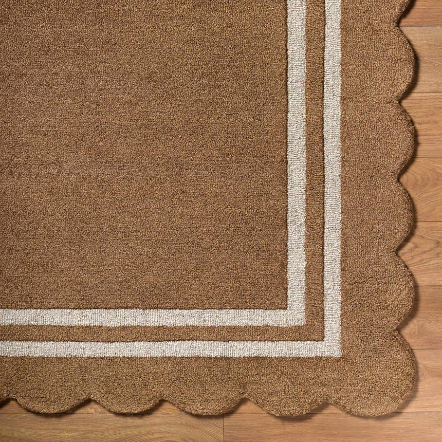 Close up of the hand tufted Chogan Umber Area Rug. 100% wool rug features a brown color, white border and scalloped edge. Corner