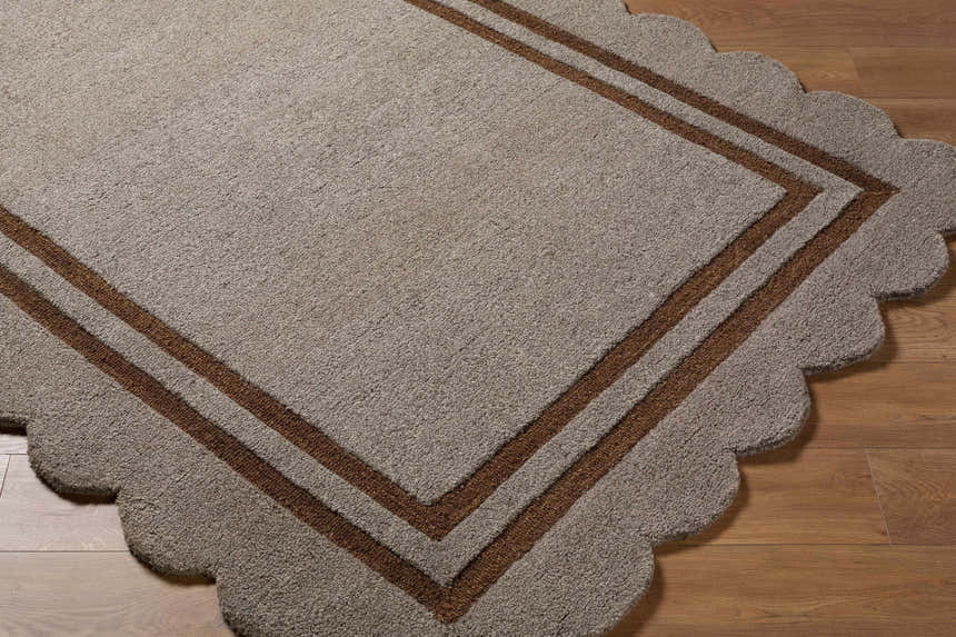Close-up of the hand-tufted Chogan Charcoal Area Rug. Details include a scalloped edge and brown border on a textured charcoal wool. Corner