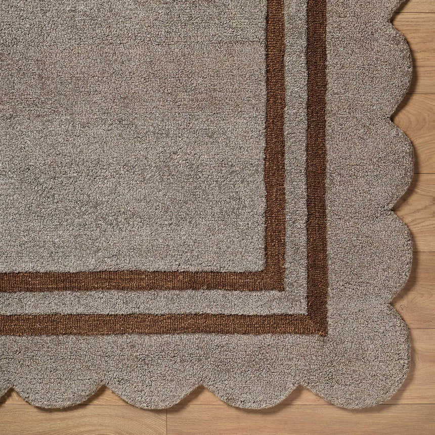 Close-up of the hand-tufted Chogan Charcoal Area Rug. Features a scalloped edge and brown striped border on a textured gray wool. Corner