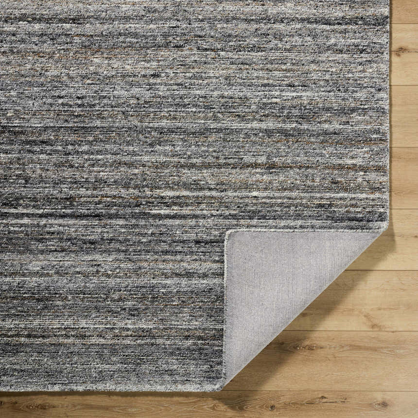 Close-up of the hand-tufted Capote Tan Area Rug showing ash, charcoal, slate blue, tan, and taupe colors and wool texture. Fold