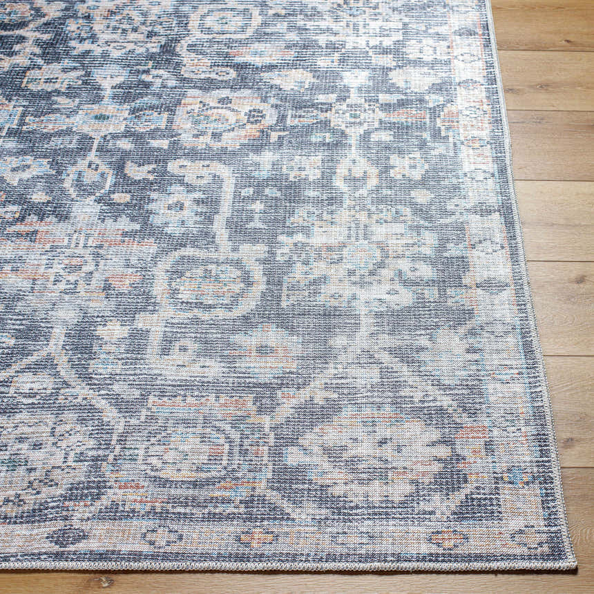 Close-up of the Eleni rug. Machine woven polyester rug in beige, black, burnt orange, denim, and gray on wood floor. Front