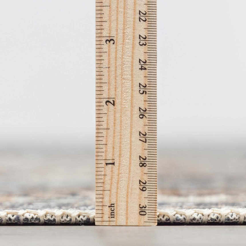 Close-up of the Dagatan Washable Area Rug showing the rug's thickness with a ruler. Beige, black, and gray oriental pattern. Pile