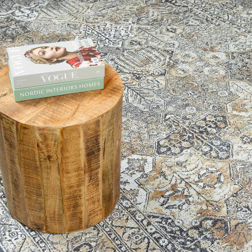 Close-up of Dagatan Washable Area Rug in beige, black, and camel with a traditional oriental pattern and a wood side table. Styleshot